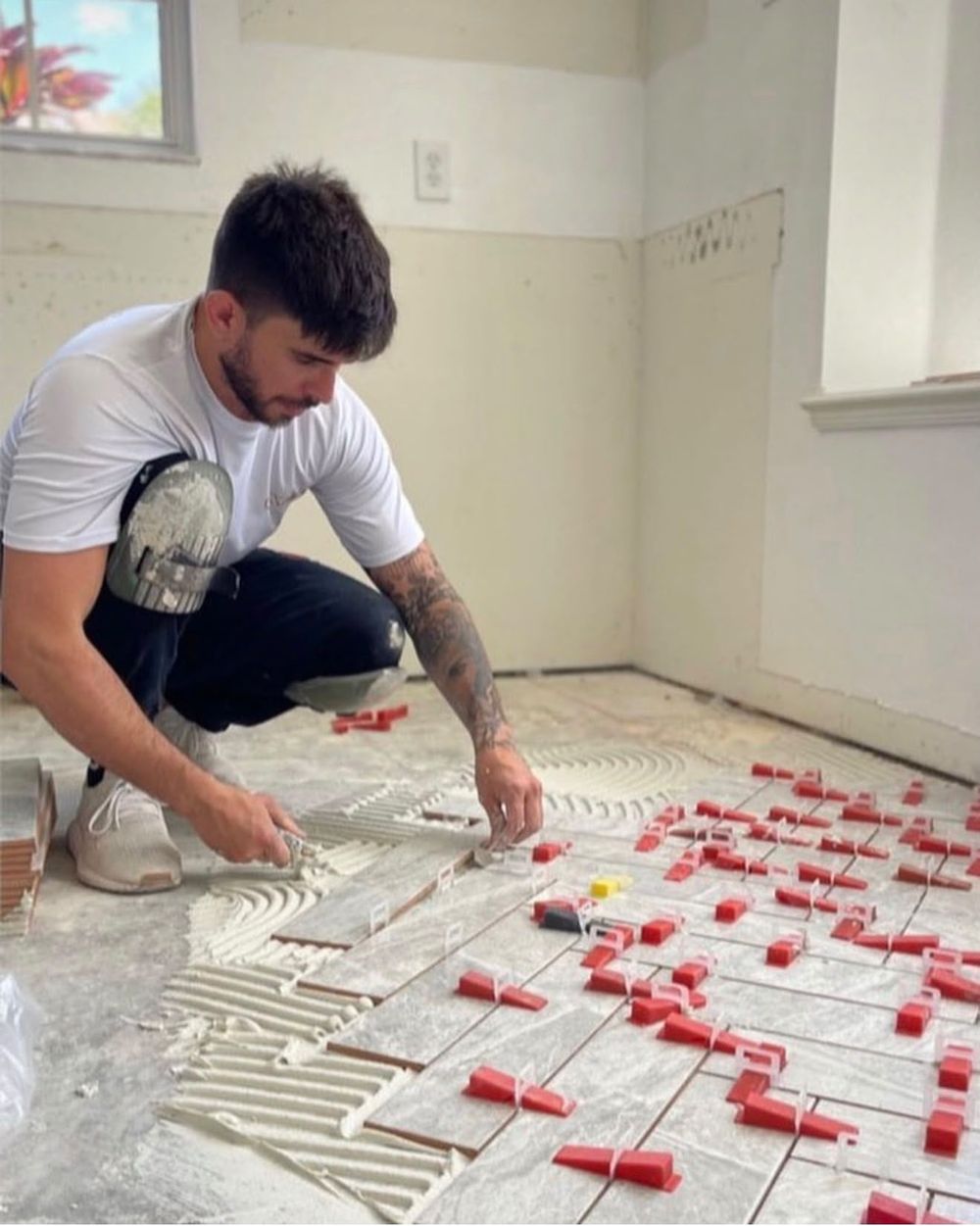 Installer setting gray floor tile with a leveling clip system on fresh thinset